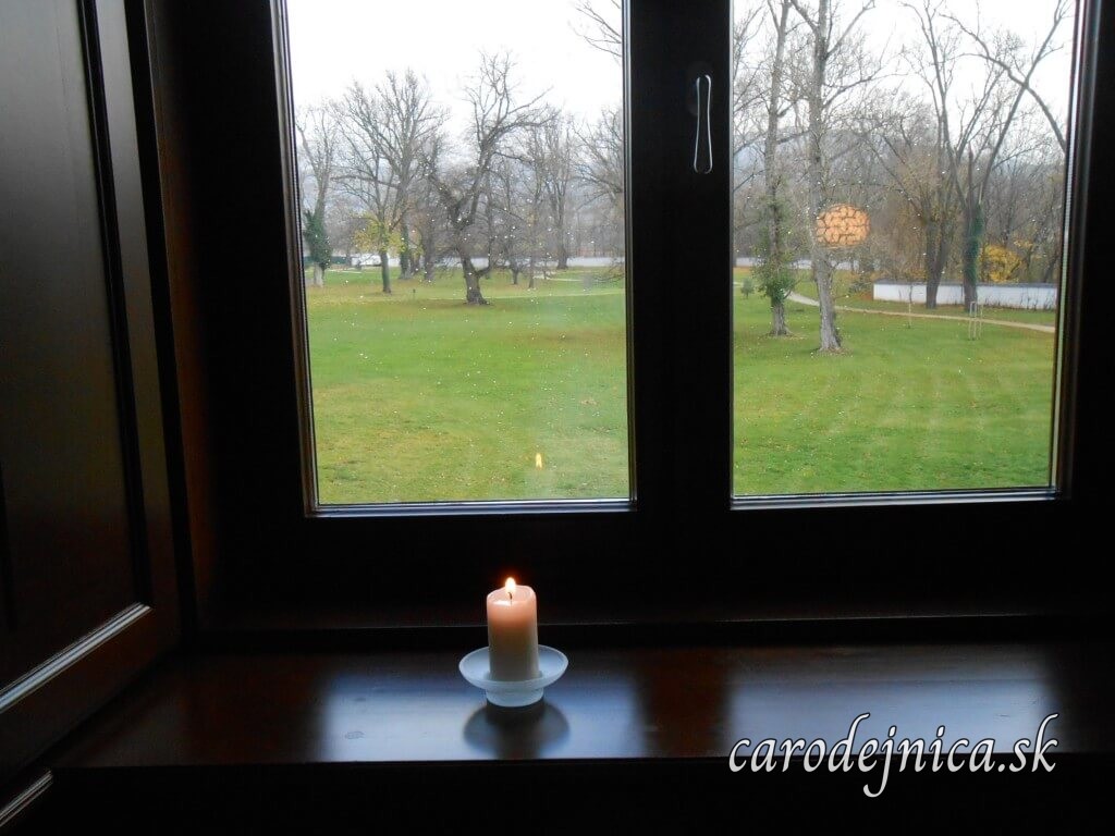 Zapálená sviečka a pohľad z okna z izby kaštieľa Oponice do upršanej záhrady