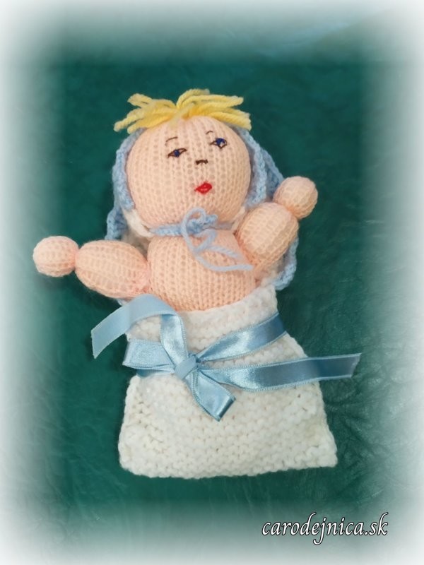 štrikovano-hačkované bábätko s modrou čiapočkou a modrou mašľou na perinke